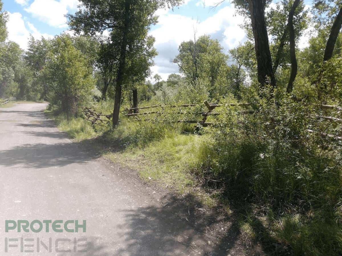 A wood fence installation in Idaho Falls of a rustic log wood stacked fence trailing down a road surrounded by untouched plants and trees.