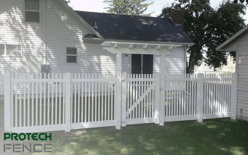 Capturing a charming scene of expert vinyl fence installation, this image showcases a dog-eared white picket vinyl fence, adorned with a matching white vinyl gate and frame in a backyard.