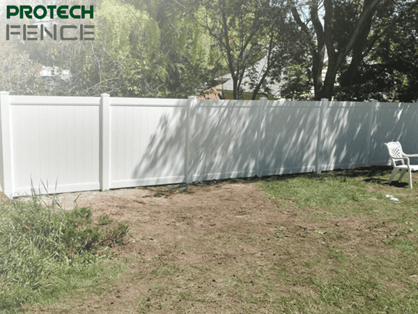 A photo of a pristine white vinyl fence running along a sidewalk, with "Protech Fence" watermarked on it, illustrating an example of vinyl fence installation cost per foot.