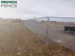 A sturdy chain-link fence installed by one of the top fence companies in Pocatello, running alongside a grassy field with the Protech Fence logo in the upper left corner.
