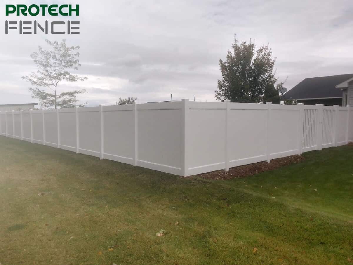 A continuous stretch of a 5 ft high vinyl privacy fence with no visible gate, bearing the logo of Protech Fence, set against a residential backdrop with overcast skies. 