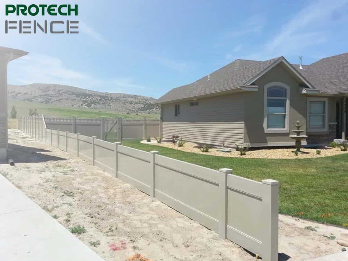 A 4 foot vinyl privacy fence extends around the perimeter of a residential yard, with the Protech Fence logo in the top left, showcasing a beige fence against a backdrop of a house and hills, providing a secure and private boundary. 