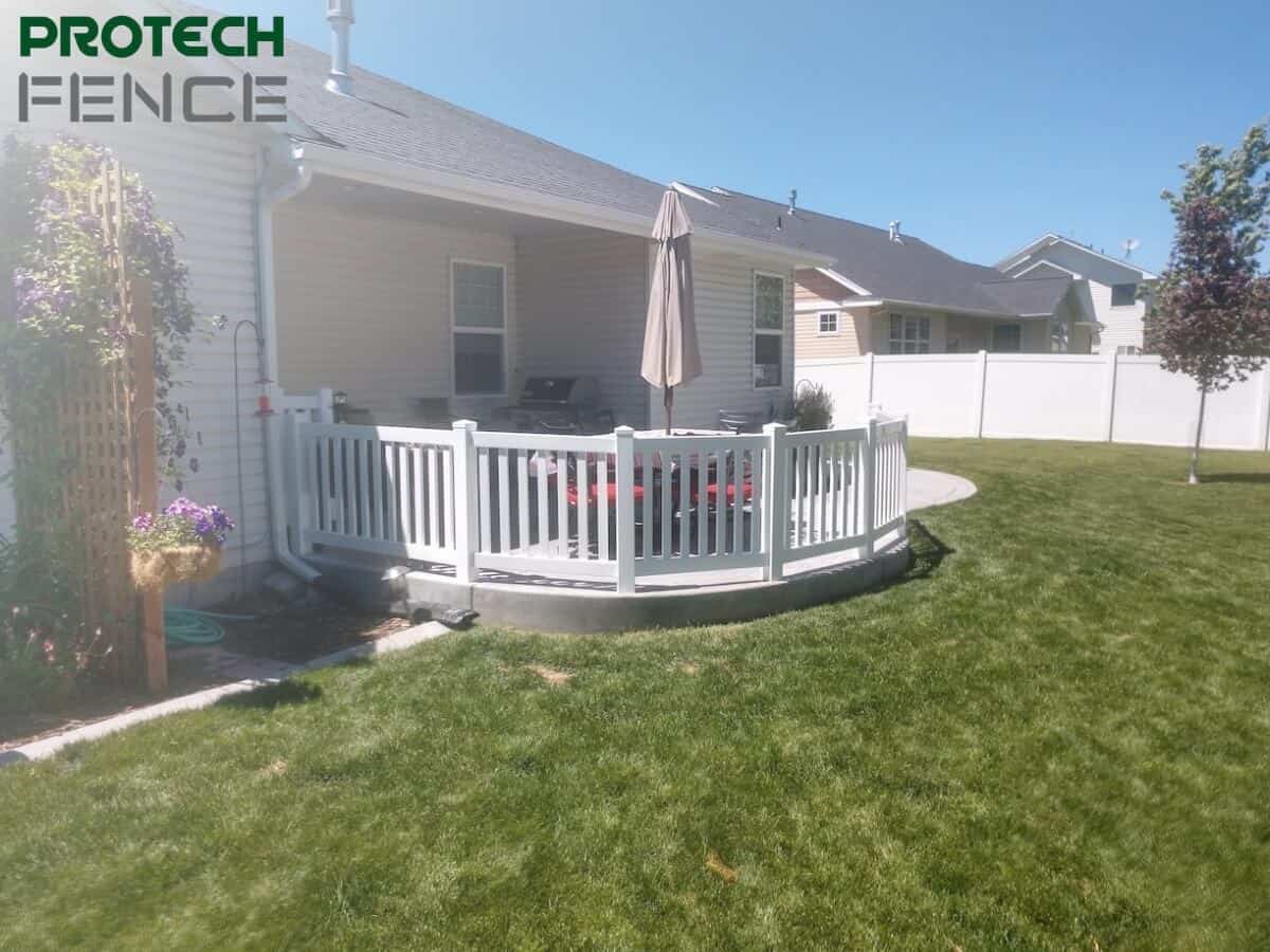 Curved deck designed by deck contractors Pocatello with white railings, encompassing an outdoor grill area in a lush backyard, showcasing Protech Fence's work on a sunny day. 