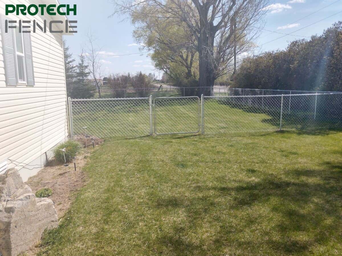 A residential chain link fence by chain link fence companies Pocatello encircles a green backyard, showcasing a secure and open area that maintains natural aesthetics while providing safety. 