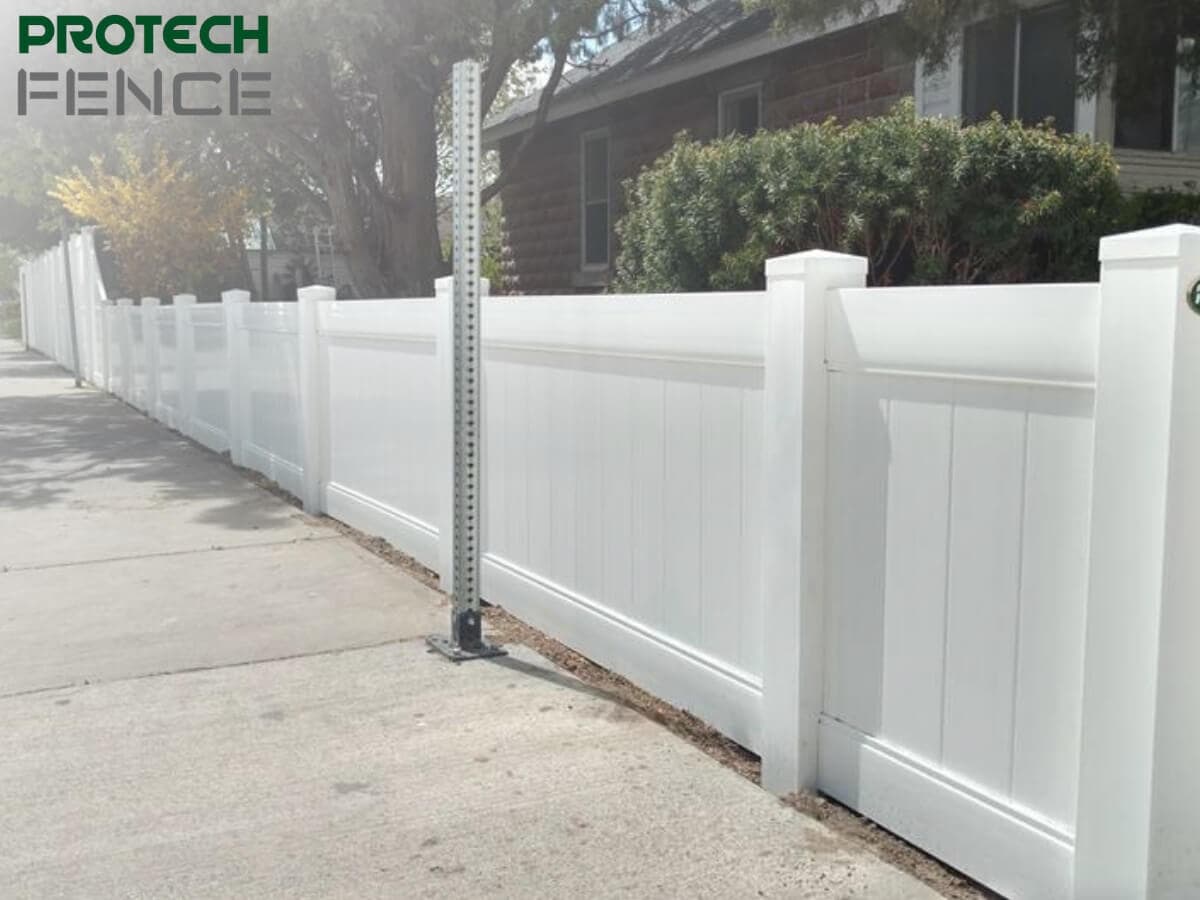 A 4 foot vinyl privacy fence with vertical paneling and caps running along a sidewalk, featuring the Protech Fence logo in the top left, illustrating the fence's clean appearance and sturdy posts against an urban backdrop. 
